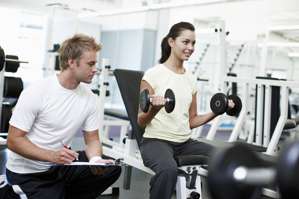 A monitorizar o progresso dela. uma jovem atraente de treinamento de peso com seu personal trainer - Foto, Imagem