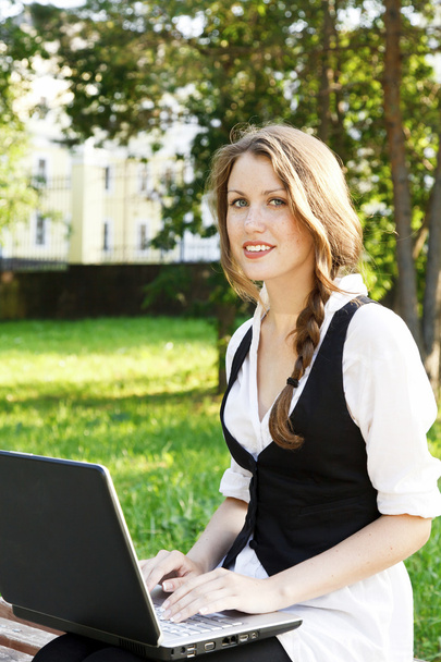 Jeune jolie femme avec ordinateur portable assis sur le banc dans un parc
. - Photo, image