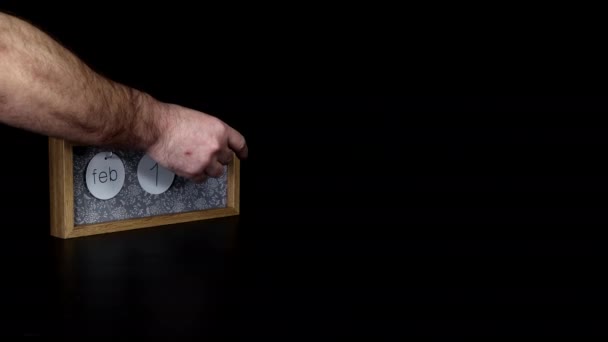 A wooden calendar block with the date of February the 14th with a mans hand putting on and taking off the metal discs with the date and month on them, with rose petals filmed in 8k quality - Metraje, vídeo