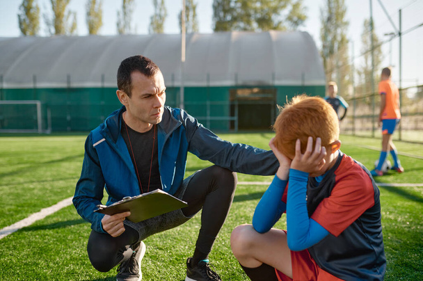 Coach comforting crying little soccer player after missed goal. Kids soccer football concept - Foto, imagen