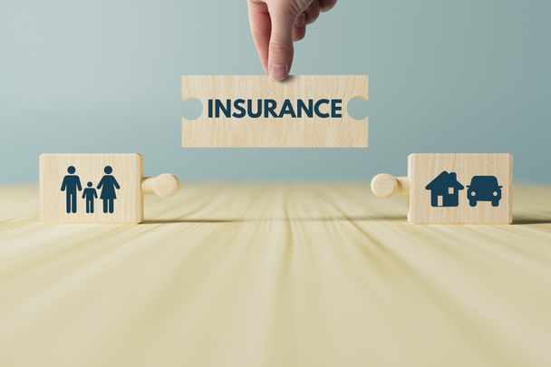 The hand holds a wooden block with an INSURANCE putting it on top of other blocks with icons of family, home, car, life. The concept of getting insured, insurance as an important element of life. - Photo, Image
