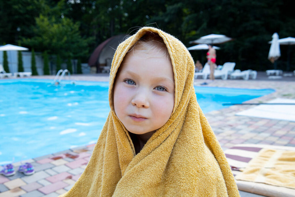 Ребенок девочка, покрытая полотенцем сидит у бассейна. - Фото, изображение