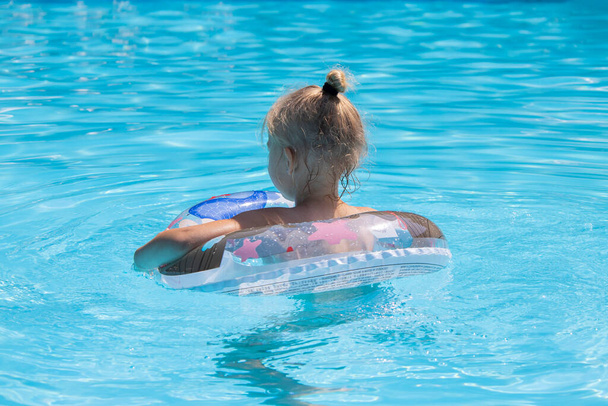 Παιδί κορίτσι κολυμπά με ένα φουσκωτό δαχτυλίδι στην πισίνα. - Φωτογραφία, εικόνα