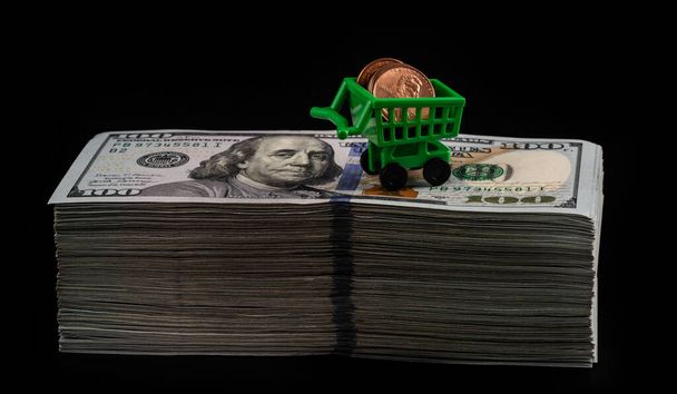 Egy miniatűr kosár 1 amerikai centes érmékkel a tetején ül egy nagy halom 100 amerikai dollár bankjegy. - Fotó, kép