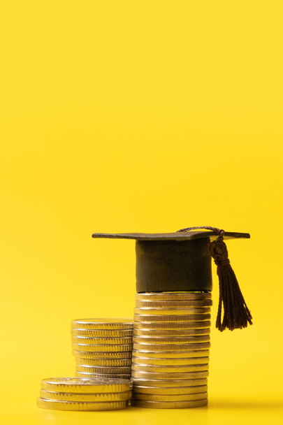 Graduated cap with coins on yellow background. Savings for education concept. - Foto, Imagen