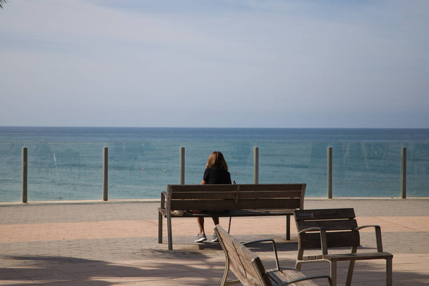 Bir bankta oturan kadın denizin ufkuna bakıyor. Kadın rahat ve nostaljik bir şekilde denize bakıyor. Rahatlama ve barışı kabul et. - Fotoğraf, Görsel