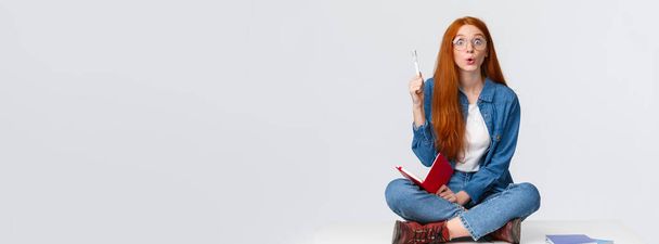 Yetenekli ve zeki kızıl saçlı genç öğrenci, ödevlerini çözen üniversiteli kız, çözümü var, planı düşünüyor, elinde defterle yerde oturuyor, Eureka 'yı yükseltiyor, düşüncelerini söylüyor.. - Fotoğraf, Görsel