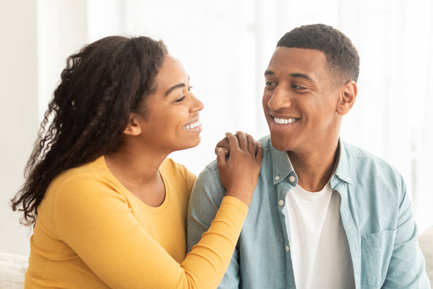 Lifestyle, romantic and date at home. Smiling pretty millennial african american wife looking at husband, enjoy tender moment at free time, sun flare, close up. Love, family relationship at home - Photo, Image