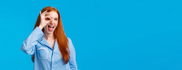 Carefree and sassy happy redhead woman with blue eyes, showing okay, no worries and satisfaction gesture over eye, look through fingers pleased, showing tongue, promote feminine hygiene products. - Photo, Image