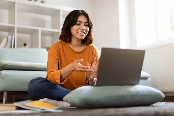 Αντίληψη τηλεδιάσκεψης. Happy Young Arab Woman Making Video Call With Laptop at Home, Χαμογελώντας Γυναίκα της Μέσης Ανατολής κάθεται στο πάτωμα, μιλώντας και χειρονομώντας στην κάμερα, απολαμβάνοντας την online επικοινωνία - Φωτογραφία, εικόνα
