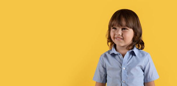 Продукты для развития детей. Счастливый мальчик смотрит в сторону на пустое пространство и улыбается, наслаждаясь предложением, оранжевый фон студии, панорама - Фото, изображение