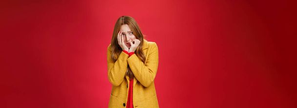 Portrait of shocked and scared insecure woman in yellow coat covering face in horror and fear biting nails squinting and looking intense left as frightened being victim standing in shook, trembling. - Photo, Image