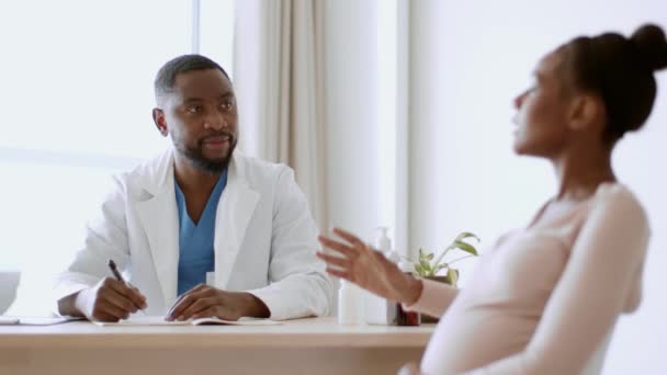 Těhotenská lékařská péče. Mladá těhotná africká americká žena sedí na návštěvě lékaře, mluví o zdravotním stavu, dává jí vitamíny předpis, sledovací injekce, zpomalený pohyb - Záběry, video