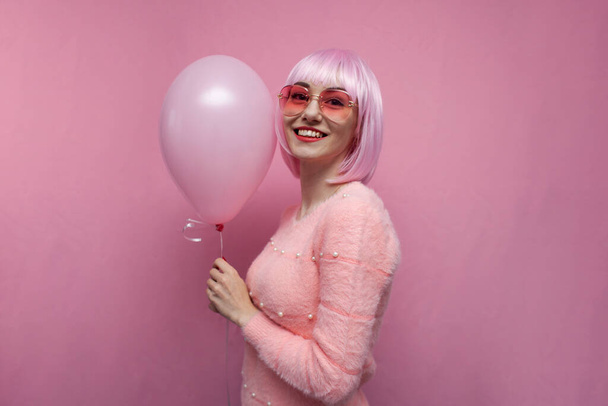 Pembe saçlı genç kız pembe bir balon tutuyor ve gülümsüyor, renkli saçlı bir hippi. - Fotoğraf, Görsel