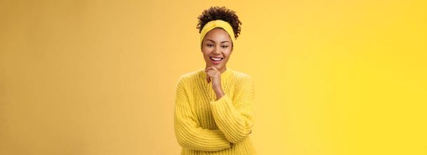 Ενδιαφέρομαι ενθουσιασμένος ενθουσιώδης όμορφος γυναίκα επιχειρηματίας κομψό πουλόβερ κεφαλόδεσμο afro χτένισμα αγγίζοντας πηγούνι στοχαστική χαμογελώντας αρέσει ιδέα του έργου στέκεται κίτρινο φόντο ιντριγκάρει. - Φωτογραφία, εικόνα