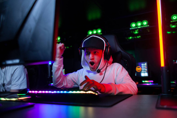 young emotional guy gamer in headphones sits in a computer club and plays a computer game, a man screaming at the monitor and rejoices in victory - Foto, Imagem