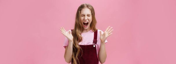 Young girl scared to death seeing spider in room yelling out loud closing eyes and opening mouth gesturing with raised hands near chest feeling afraid and insecure posing against pink background. Copy - Photo, Image