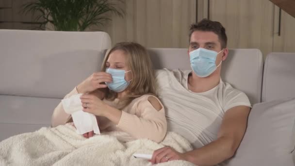 CLOSE UP: Прекрасна пара відпочиває на зручному дивані і переживає сезонний холод. Зимові застуди та грип поширюються навколо. Молодий хлопець і леді знаходяться на лікарняній відпустці, покриті ковдрою і дивитися телевізор
. - Кадри, відео