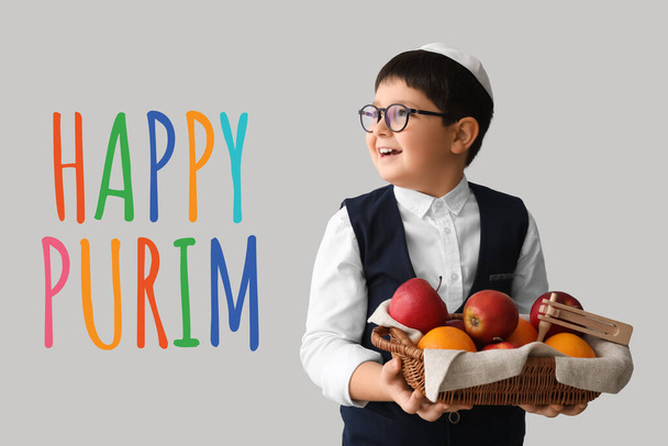 Little Jewish boy with gragger for Purim holiday and fruits in basket on light background - Foto, afbeelding