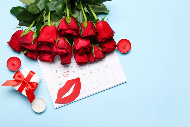 Calendar with marked date of Valentine's Day, paper lips, roses, gift and candles on blue background - Foto, Imagen