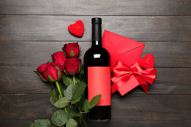 Red roses, envelope, bottle of wine and candles on dark wooden background. Valentine's Day celebration - Fotografie, Obrázek