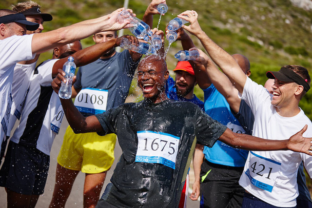A győztes kapja a zsákmányt. Egy csapat fiatal férfi vizet öntött a barátjára, miután lefutottak egy maratont. - Fotó, kép