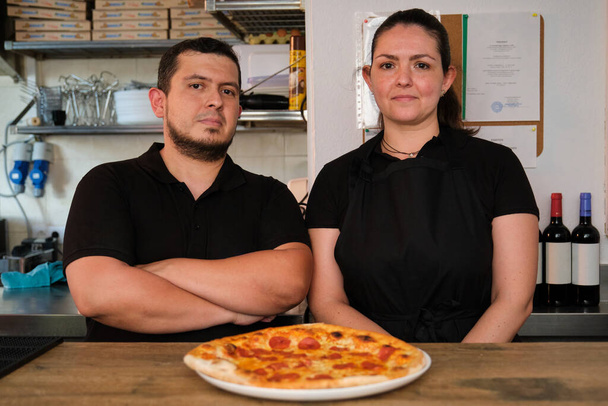 Restaurant owners looking at camera with a freshly baked pepperoni pizza. Pizzeria. - Foto, imagen