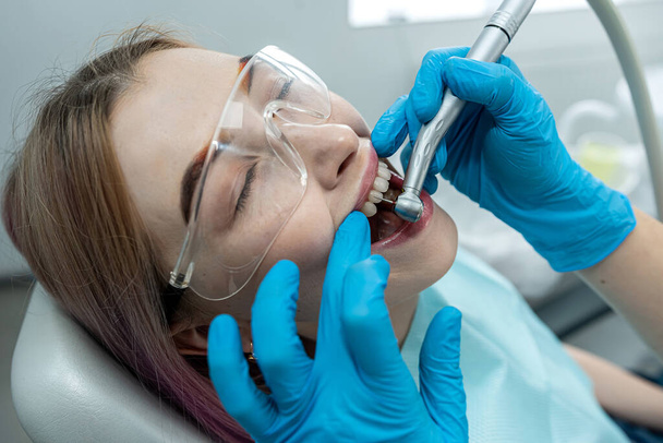 Ein junges Mädchen sitzt in einem Behandlungsstuhl, während ein Zahnarzt ihre Zähne in einer Zahnklinik behandelt. gesunde Mundhöhle. Zahnbehandlung - Foto, Bild