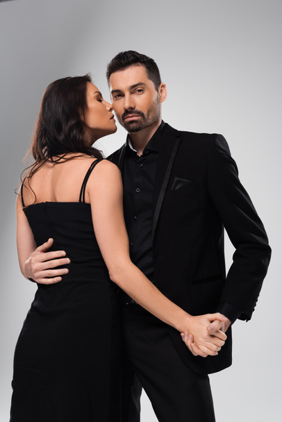 bearded man in formal wear holding hands with girlfriend in black dress isolated on grey  - Photo, Image