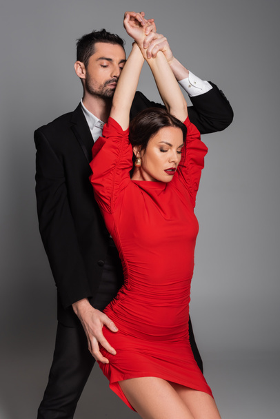 Parrakas mies koskettaa käsiä ja lonkka seksikäs tyttöystävä punainen mekko eristetty harmaa  - Valokuva, kuva