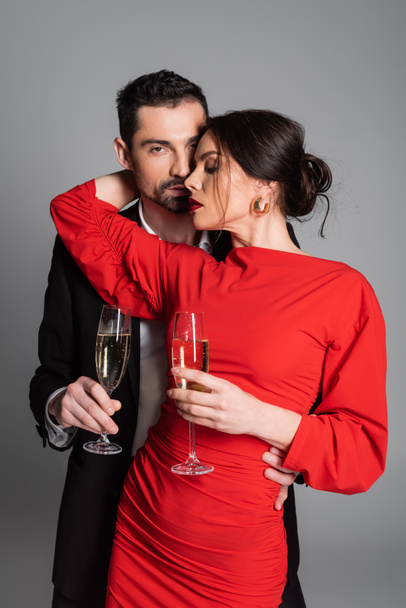 Passionate man holding champagne and hugging girlfriend in dress on grey background  - Foto, Imagem