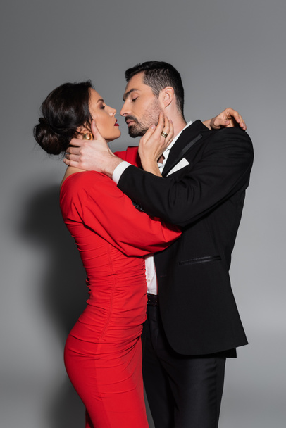 Side view of sexy woman in dress kissing elegant boyfriend on grey background  - Фото, зображення