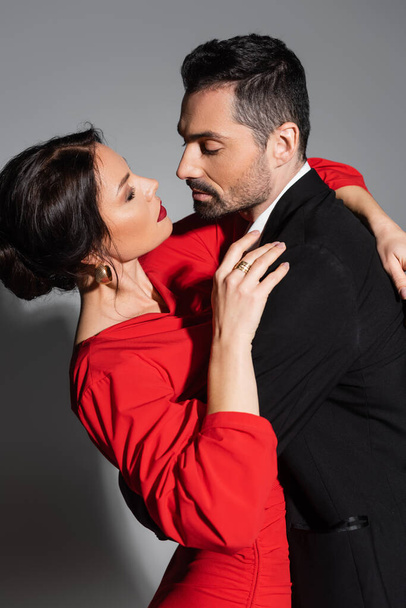 Sensual brunette woman hugging boyfriend in suit on grey background  - Fotografie, Obrázek