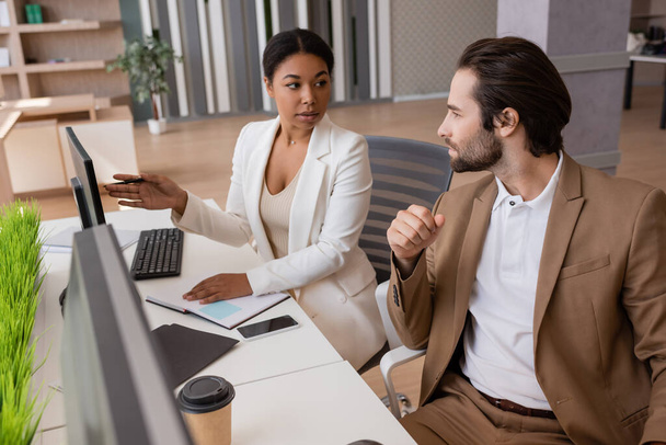 multiracial businesswoman pointing at computer monitor and talking to colleague in office - Foto, Imagem