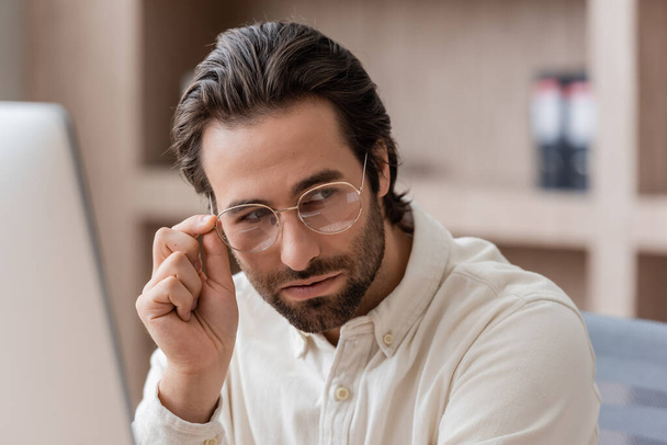 young bearded businessman in white shirt adjusting eyeglasses and looking away in office - Fotografie, Obrázek