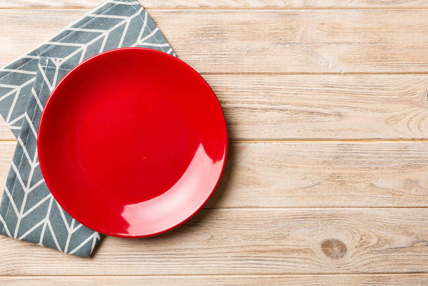 Visão superior sobre fundo colorido vazio redondo prato vermelho na toalha de mesa para alimentos. Prato vazio no guardanapo com espaço para o seu design. - Foto, Imagem