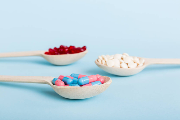 Vitamin capsules in a spoon on a colored background. Pills served as a healthy meal. Red soft gel vitamin supplement capsules on spoon. - 写真・画像