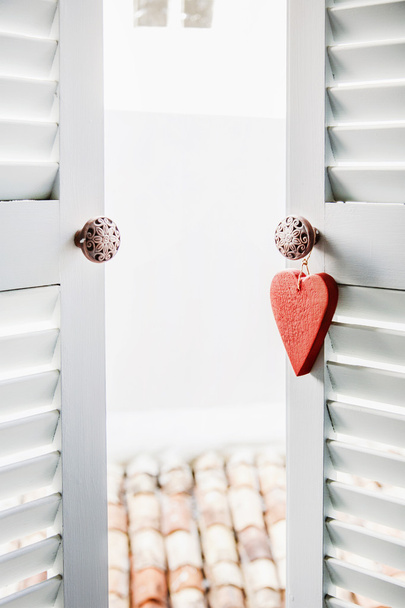 Coeur en bois rouge suspendu à la fenêtre blanche de la terrasse
 - Photo, image