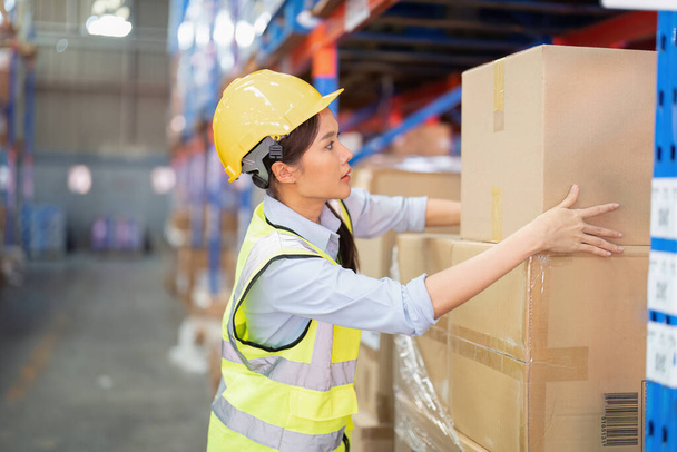 Staff working in large depot storage warehouse lift up heavy carton box to shelf - Фото, изображение