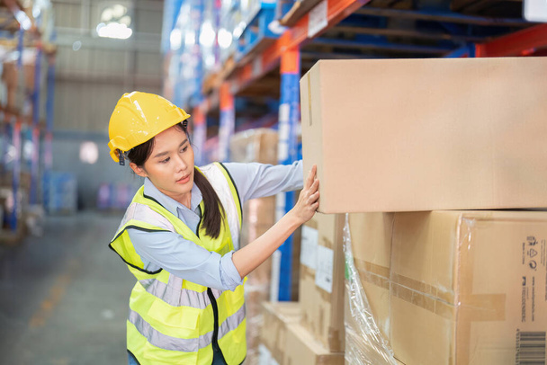 Staff working in large depot storage warehouse lift up heavy carton box to shelf - Foto, imagen