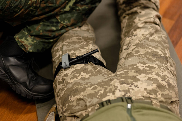 Egy katona harci orvosi érszorítót használ, hogy megállítsa a vért az elsősegély alatt. Utasítások harci taktikai felszereléshez. Kiváló minőségű fénykép - Fotó, kép