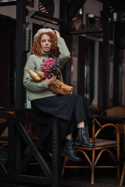 Frauenporträt im Baskenmützenpullover mit einem Blumenstrauß im Hintergrund des Restaurants  - Foto, Bild