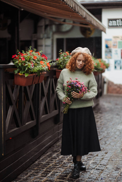 Женский портрет в беретском свитере с букетом цветов на заднем плане ресторана  - Фото, изображение