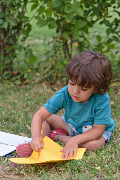 Ребенок из начальной школы лежит на траве и делает домашнее задание. - Фото, изображение