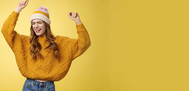 Oh yeah party vibe. Portrait joyful carefree dancing happy girl wearing winter hat sweater having fun raising hands up dancing moving music rhythm celebrating success positive news. Copy space - Photo, Image