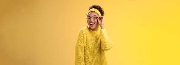 Чарівна стильна впевнена красива афро-американська радісна дівчина-підліток торкається окулярів ніс сміється широко дивіться вниз правого кута посмішка весело жартує насолоджуючись, жовтий фон
. - Фото, зображення