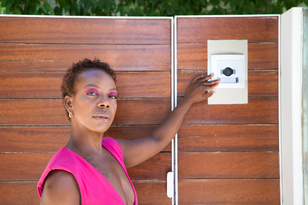 Young, beautiful Afro American woman calling the electronic doorman at the entrance of a luxury flat. - Photo, Image