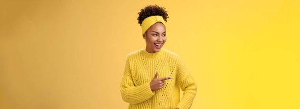 Entspannte moderne Millennial afrikanisch-amerikanische Mädchen zeigen interessante lustige Promo zeigt linke Zeigefinger kichernd halten Handtasche selbstbewusste lässige Pose, stehen gelben Hintergrund reden. - Foto, Bild