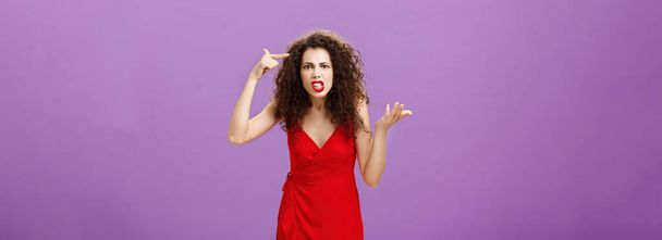 Outraged and pissed wife critisize dumb idea, outraged and fed up with stupid husband actions rolling finger near temple gesturing with raised palm, being angry and questioned over purple background. - 写真・画像