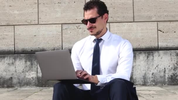 若いビジネスマンは彼のコンピュータと屋外で働いている。男はオフィスに行く前に階段に座っている. - 映像、動画
